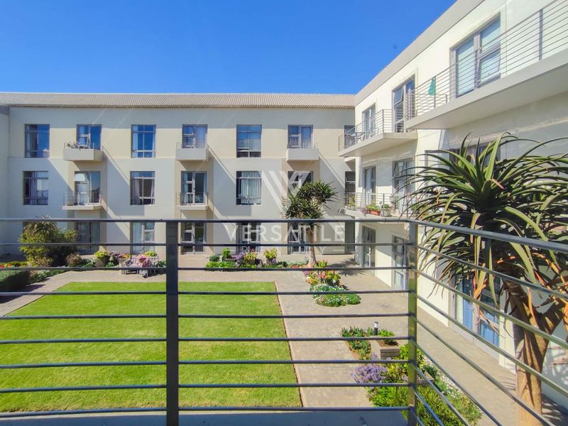 View from a balcony overlooking a well-maintained communal courtyard with a lawn, paved pathways, and the surrounding retirement village building facade.