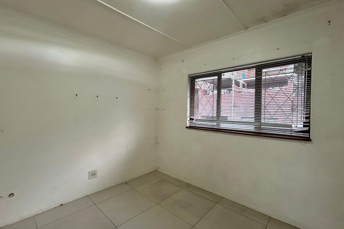 A vacant bedroom featuring tiled flooring, a window with security bars and blinds, and plain white walls requiring cosmetic attention.
