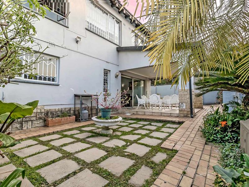 Rear exterior view of the townhouse featuring a covered patio, stone-clad base, and a paved garden area with established landscaping.