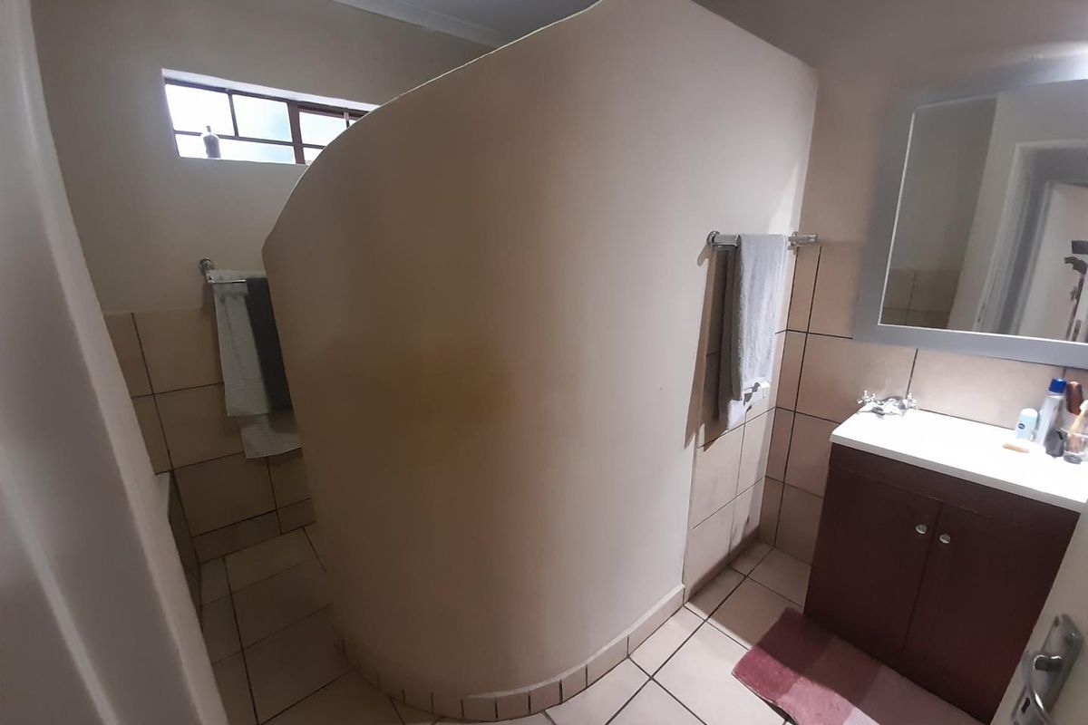 A functional bathroom featuring a curved privacy wall, tiled flooring, a vanity cabinet with basin, and a wall-mounted mirror.