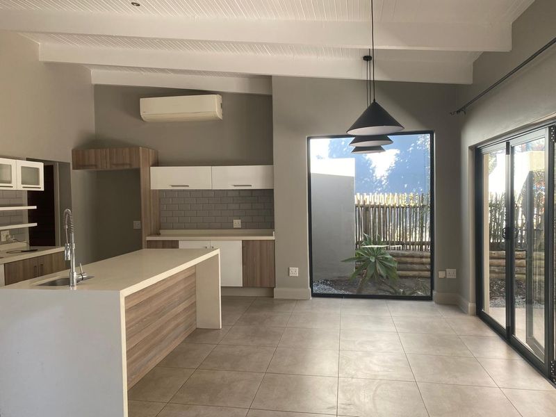 Modern open-plan kitchen and living area featuring a central island, sleek cabinetry, subway tile backsplash, and large windows providing natural light and garden views.