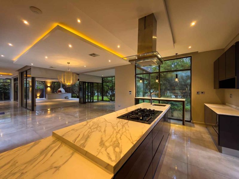 Spacious open-plan kitchen and living area featuring a marble island, gas hob, modern cabinetry, and expansive windows overlooking the garden.