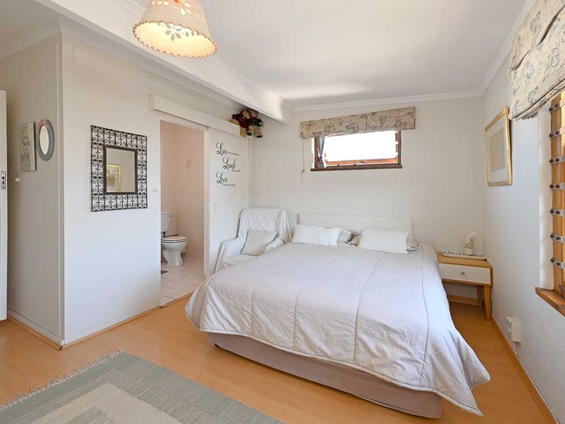 A bedroom featuring laminate flooring, a timber-framed window, and an adjoining en-suite bathroom with a sliding door entrance.
