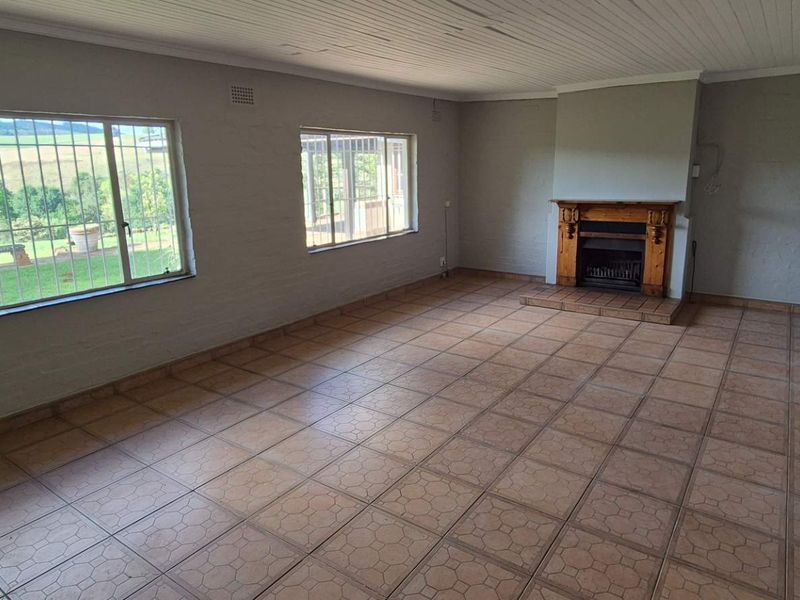Spacious, empty living room featuring tiled flooring, a traditional fireplace, and large windows with security bars, offering a blank canvas for renovation.