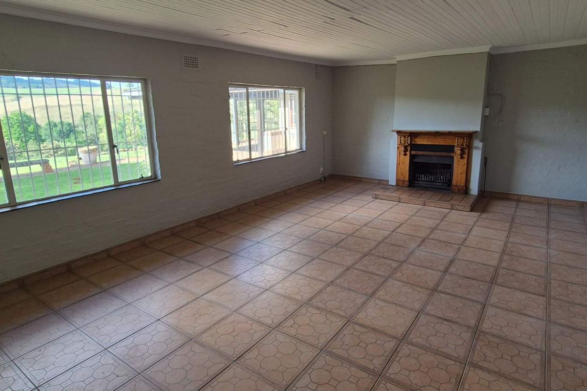 Spacious, empty living room featuring tiled flooring, a traditional fireplace, and large windows with security bars, offering a blank canvas for renovation.
