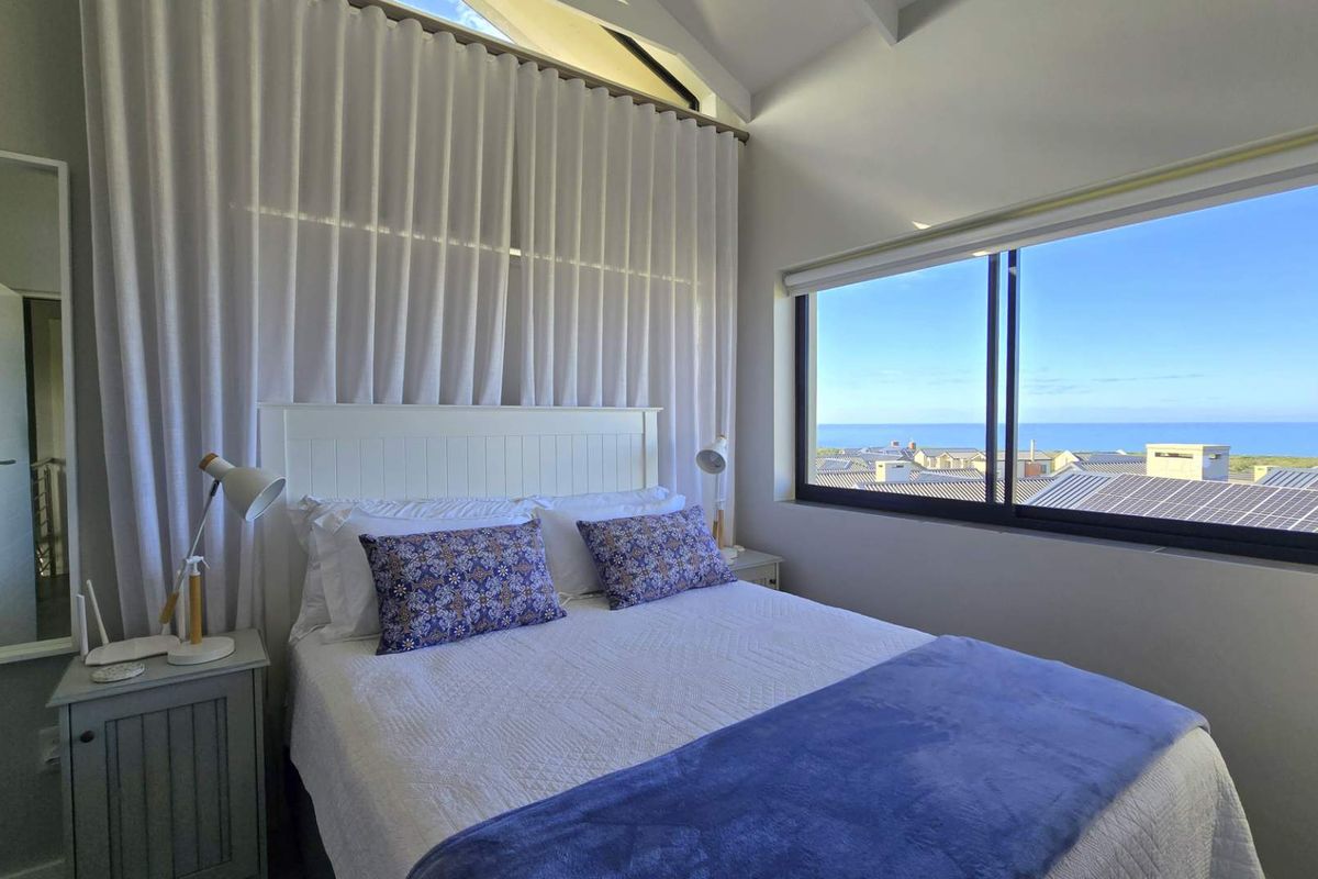 A bright bedroom featuring high vaulted ceilings, large windows with ocean views, and a neutral color palette.
