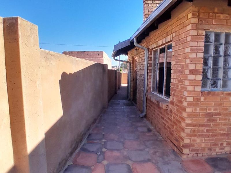 A side exterior walkway featuring face brick walls, a glass block window, and paved flooring along the side of the property.