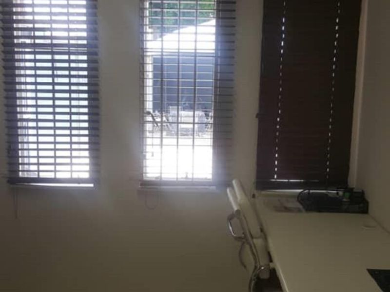A functional office space featuring tiled flooring, a built-in desk, and multiple windows fitted with venetian blinds.