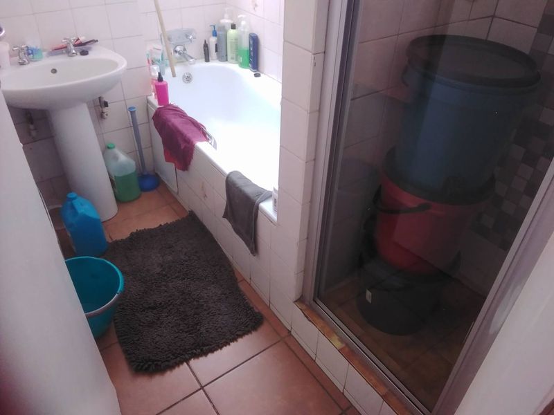 A compact bathroom featuring a pedestal basin, bathtub, and a separate shower enclosure with tiled finishes throughout.