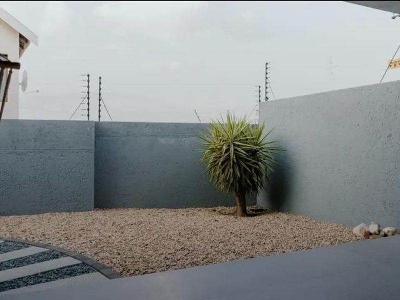 A private outdoor patio area featuring a gravel garden, paved pathway, and secure boundary walls with electric fencing.