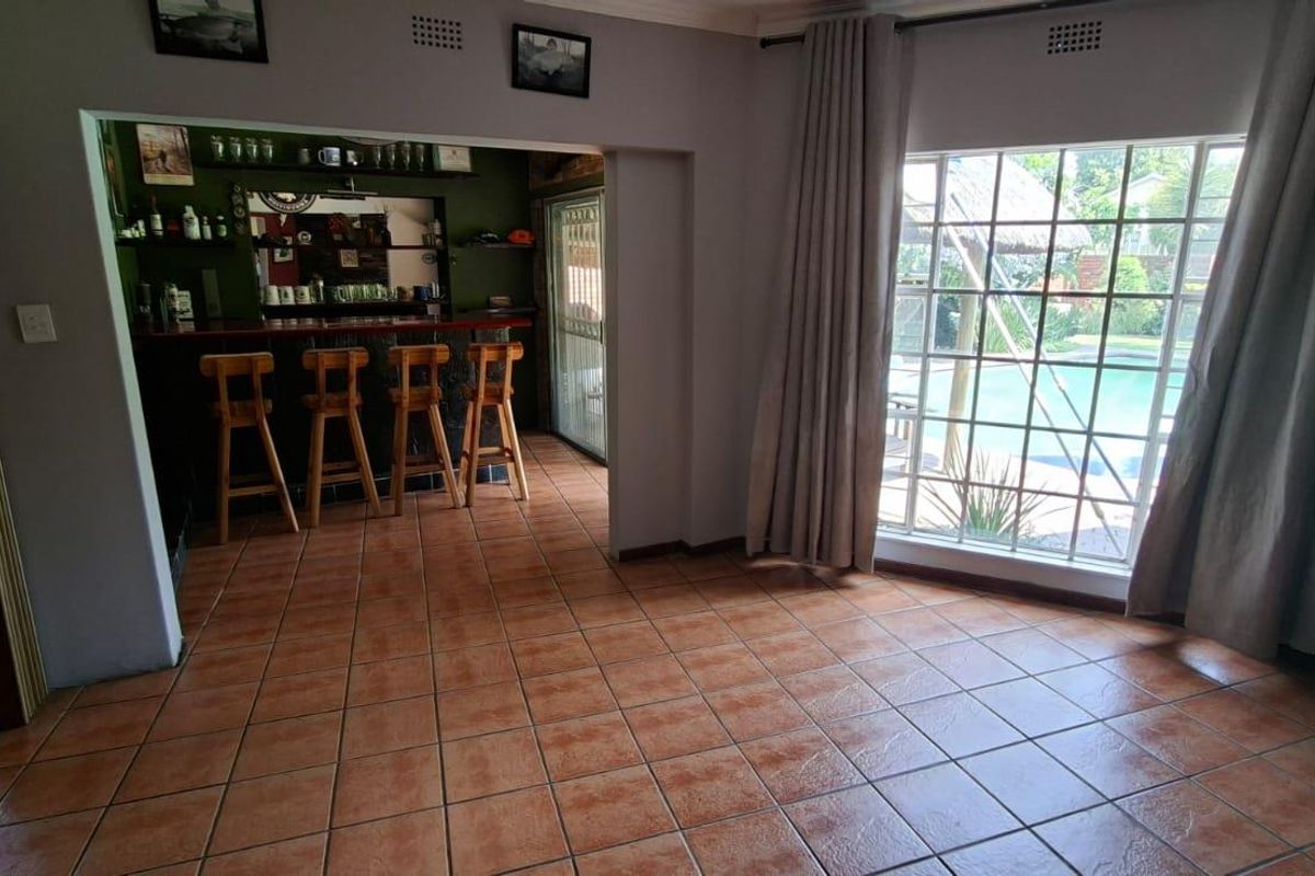A living area featuring tiled flooring, a built-in bar area, and large windows providing views of the outdoor pool area.