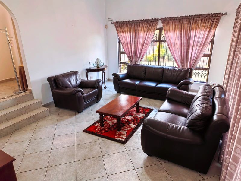 A spacious living room featuring tiled flooring, an arched entryway, and large windows with security bars, offering a bright and functional living space.