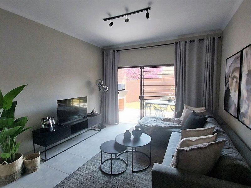 A well-maintained living room featuring modern tiled flooring, track lighting, and a large sliding glass door providing access to the outdoor patio area.