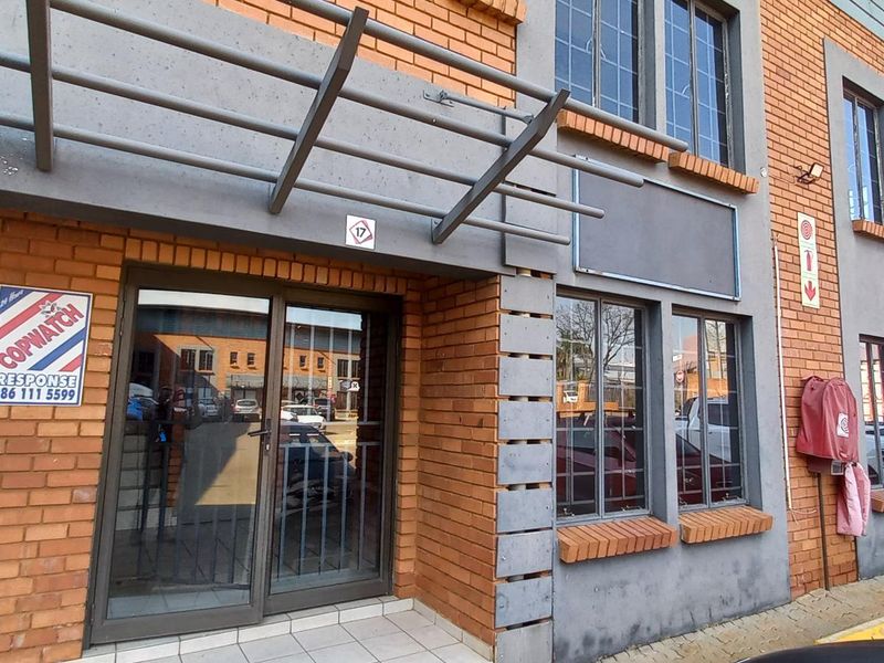Front entrance of an industrial building featuring brick facade, metal awning, and glass-paneled doors with security bars.