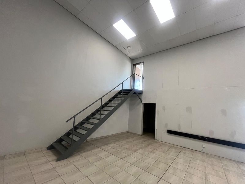 An empty commercial utility space featuring tiled flooring, a metal staircase leading to an upper level, and a suspended ceiling with recessed lighting.