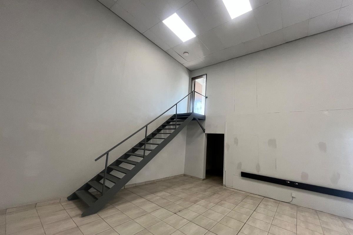 An empty commercial utility space featuring tiled flooring, a metal staircase leading to an upper level, and a suspended ceiling with recessed lighting.