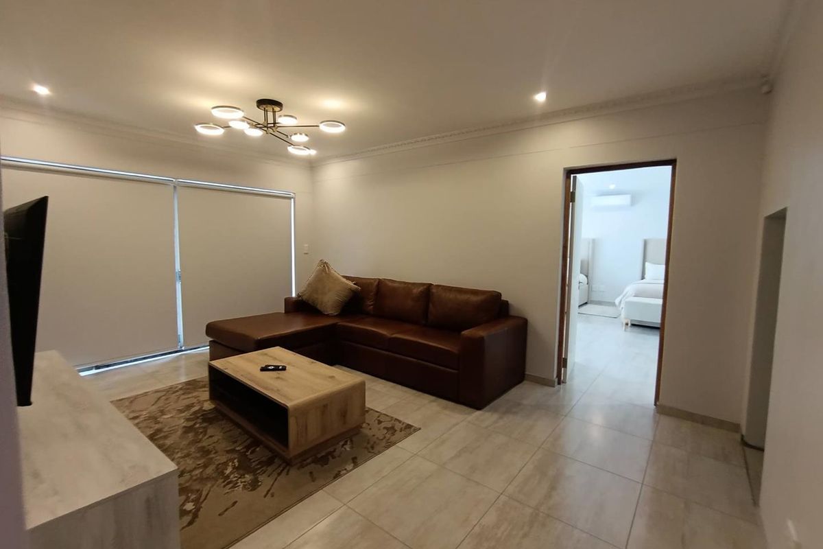 A bright and modern living room featuring large format floor tiles, recessed downlighting, and a contemporary chandelier, with direct access to an adjacent bedroom.