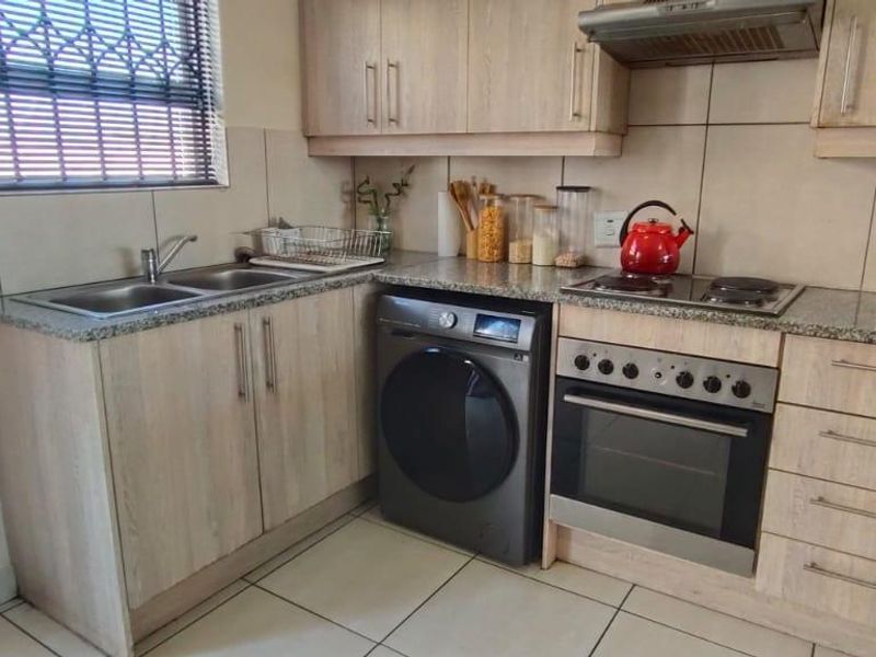 A functional kitchen featuring light wood-finish cabinetry, granite countertops, a built-in oven with hob, and a double basin sink with tiled splashback.
