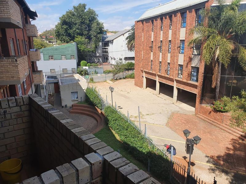 An elevated view overlooking a communal brick-paved courtyard area between apartment buildings, featuring security fencing and established landscaping.