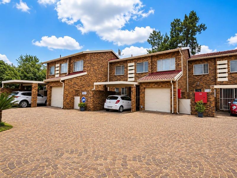 Front elevation of a townhouse complex featuring face brick construction, tiled roofs, paved driveway, and integrated garage and carport parking.
