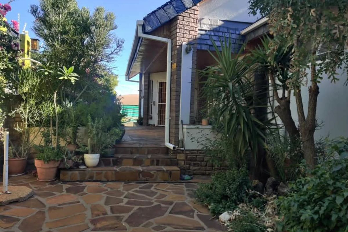 A view of the rear exterior featuring a stone-paved patio area, brick facade, and established garden surroundings.