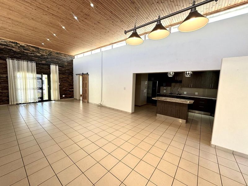 Spacious open-plan living area featuring a timber-clad vaulted ceiling, stone feature wall, and a modern kitchen with granite countertops and an island.