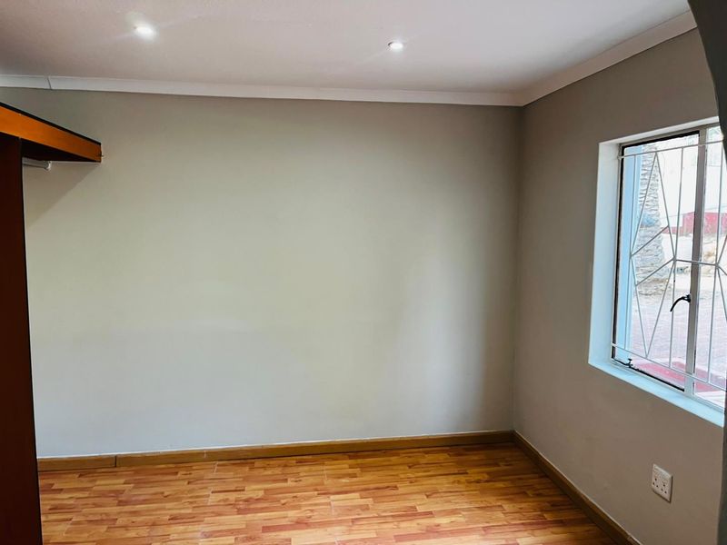 An empty bedroom featuring laminate flooring, recessed downlighting, and a window fitted with security burglar bars.