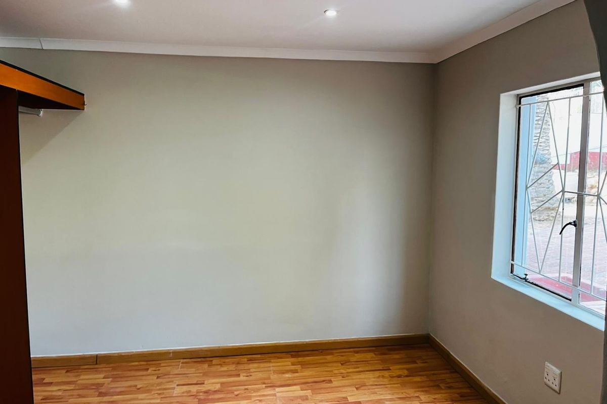 An empty bedroom featuring laminate flooring, recessed downlighting, and a window fitted with security burglar bars.