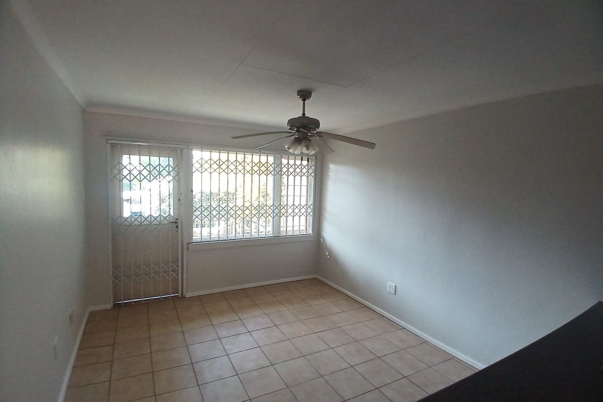 A bright, empty living area featuring tiled flooring, a ceiling fan, and security gates on the door and window.