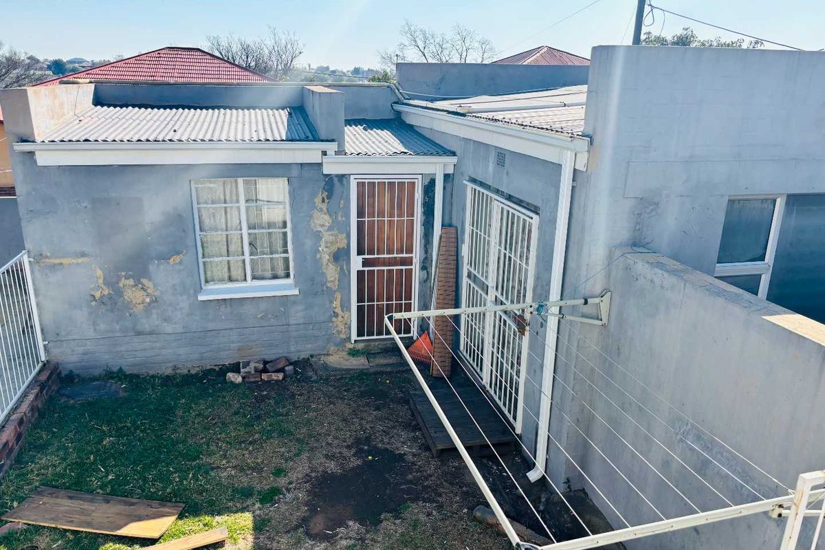 Rear exterior view of the property showing plastered walls with visible paint deterioration, security gates, and a wall-mounted clothesline in the backyard area.
