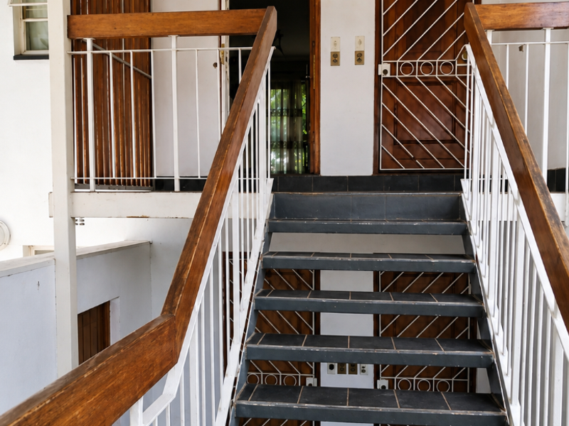 Exterior staircase leading to apartment entrance, featuring tiled steps, timber handrails, and security gates.