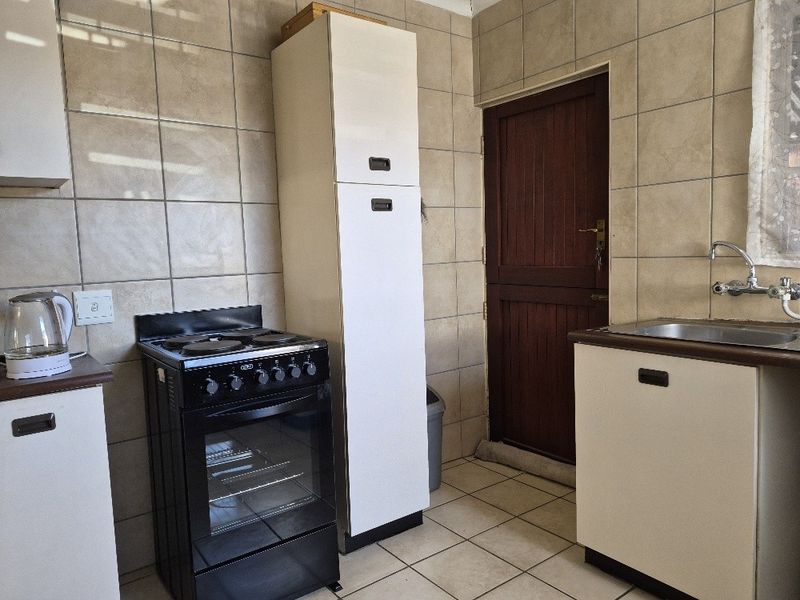 A functional kitchen featuring tiled walls and flooring, built-in cabinetry, a stainless steel sink, and a freestanding stove with direct access to an exterior door.