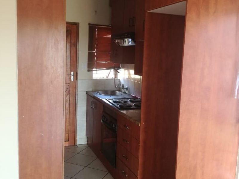 A compact kitchen featuring wooden cabinetry, a built-in oven and hob, and tiled flooring. The space is functional but shows signs of wear.