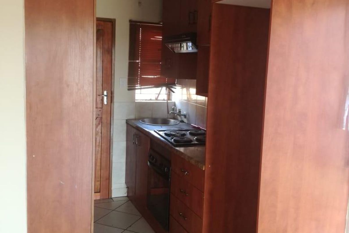 A compact kitchen featuring wooden cabinetry, a built-in oven and hob, and tiled flooring. The space is functional but shows signs of wear.