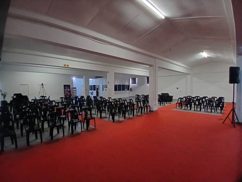 A large, open-plan event space or clubhouse featuring high ceilings, support columns, and red carpeting, suitable for various business or community gatherings.