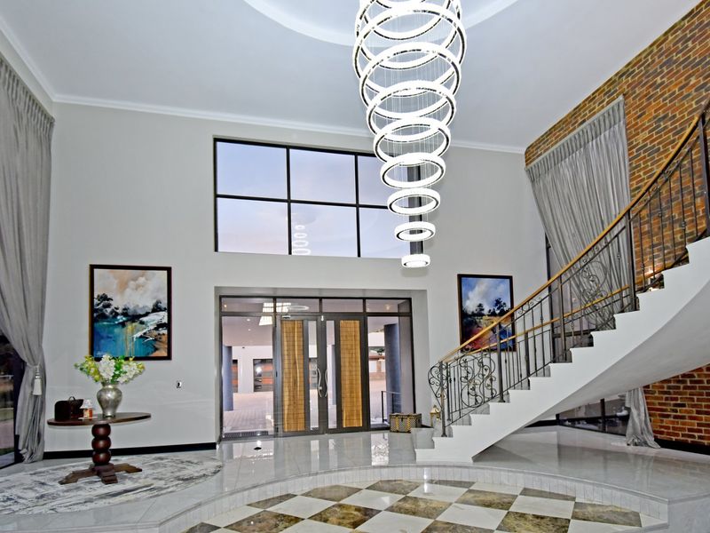 Impressive double-volume entrance hall featuring a grand staircase with wrought iron balustrade, a striking feature chandelier, and elegant tiled flooring.