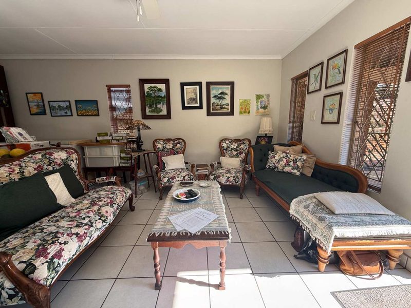 A spacious living room featuring ceramic floor tiles, a ceiling fan, and large windows fitted with venetian blinds and security gates.