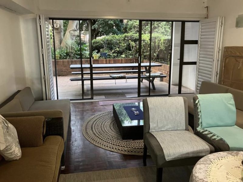 A living room featuring parquet flooring and large sliding glass doors that open onto a private patio area with a brick retaining wall.