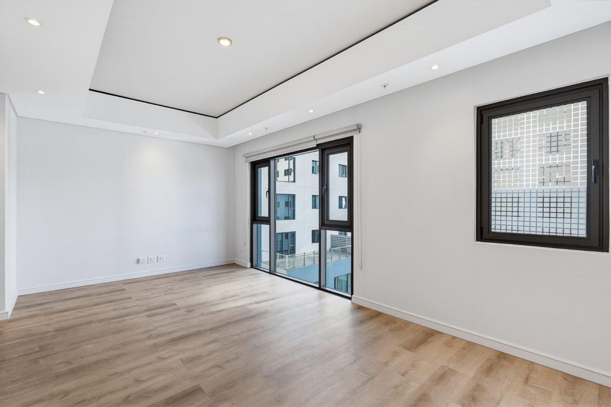 A bright, modern, and empty bedroom featuring light wood-look laminate flooring, a contemporary drop ceiling with recessed lighting, and large aluminium-framed windows.