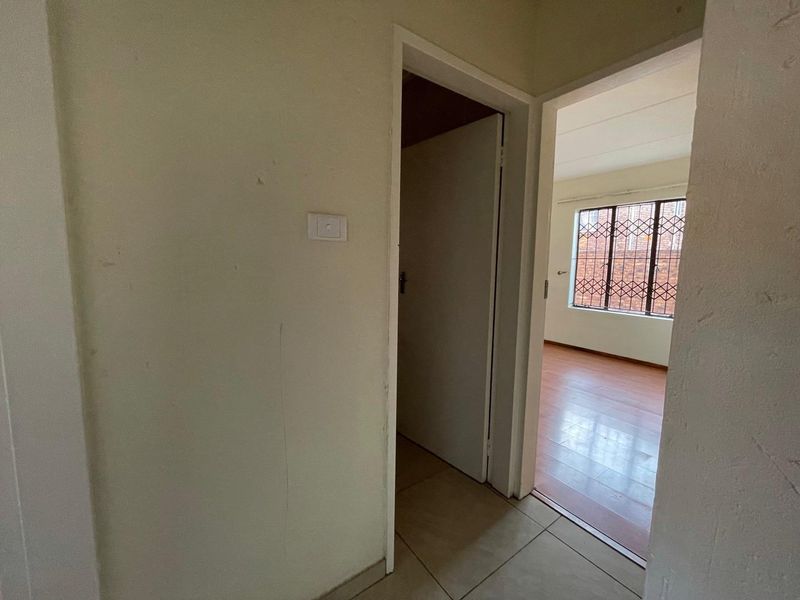 A view from a tiled hallway looking into an empty bedroom featuring laminate flooring and a window with security bars.