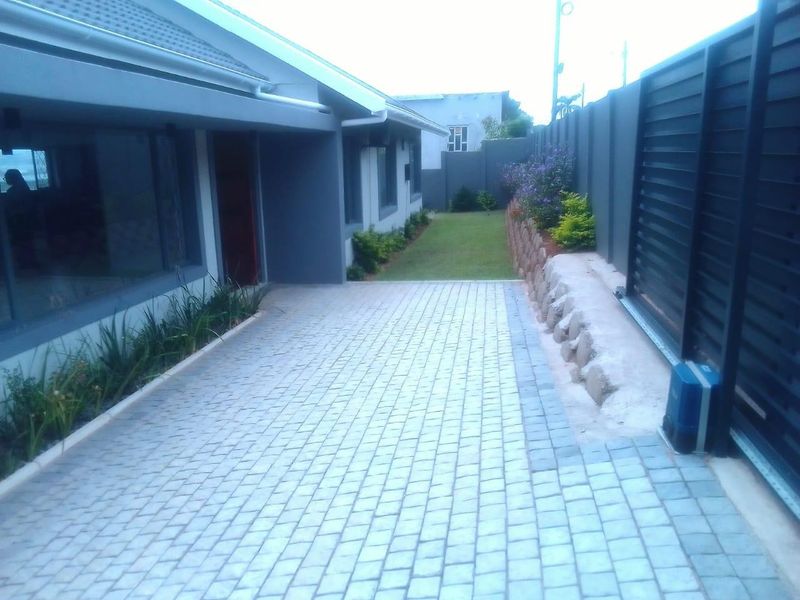 A well-maintained paved driveway leading to the side of the house, featuring a modern sliding gate, retaining wall, and neat garden borders.