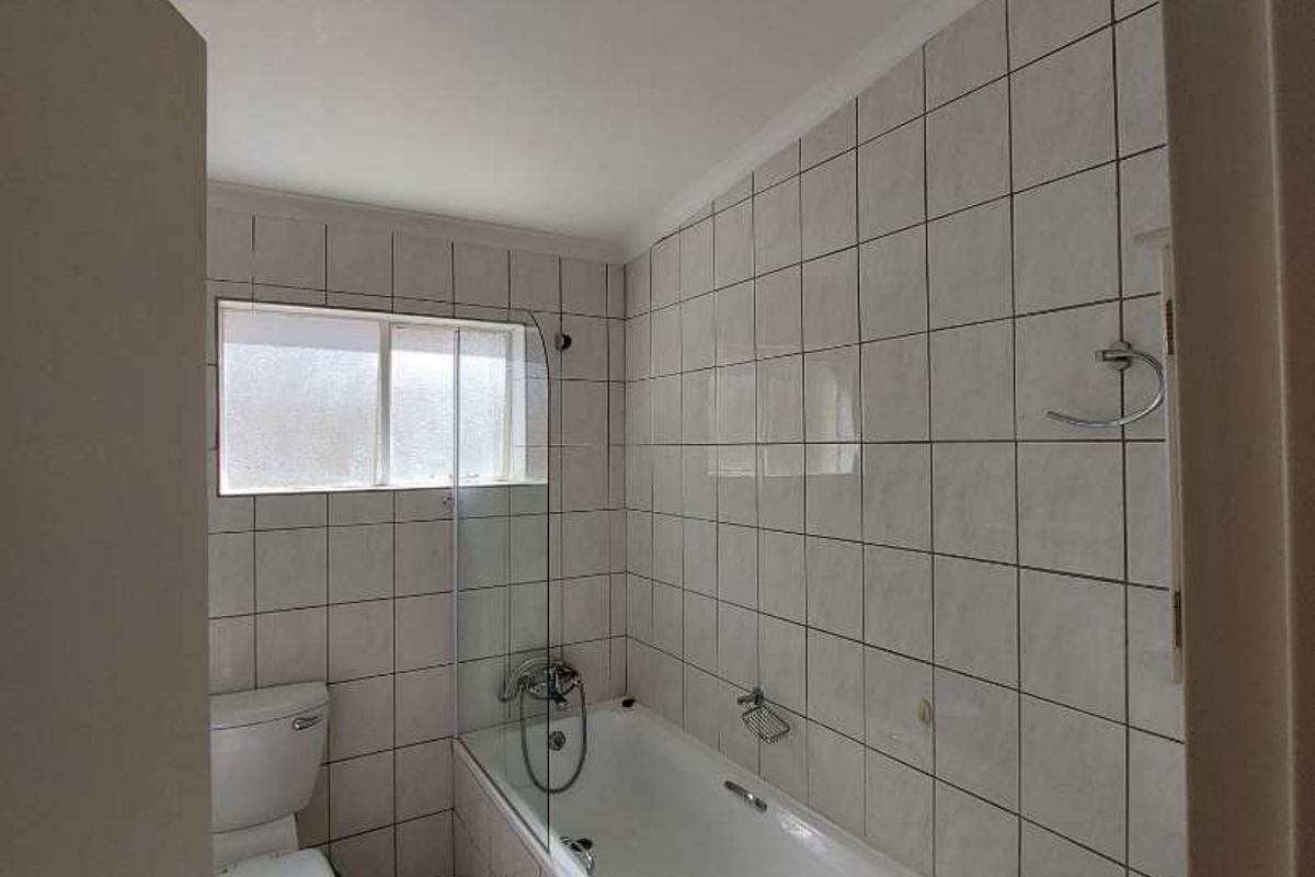 A functional bathroom featuring a built-in bathtub with shower mixer, tiled walls, and a standard toilet.