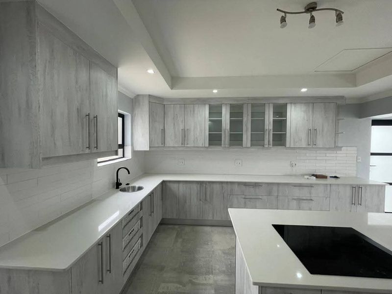 Modern kitchen featuring light wood-grain cabinetry, white stone countertops, a central island with a built-in hob, and a sleek subway tile backsplash.