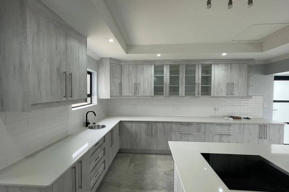 Modern kitchen featuring light wood-grain cabinetry, white stone countertops, a central island with a built-in hob, and a sleek subway tile backsplash.
