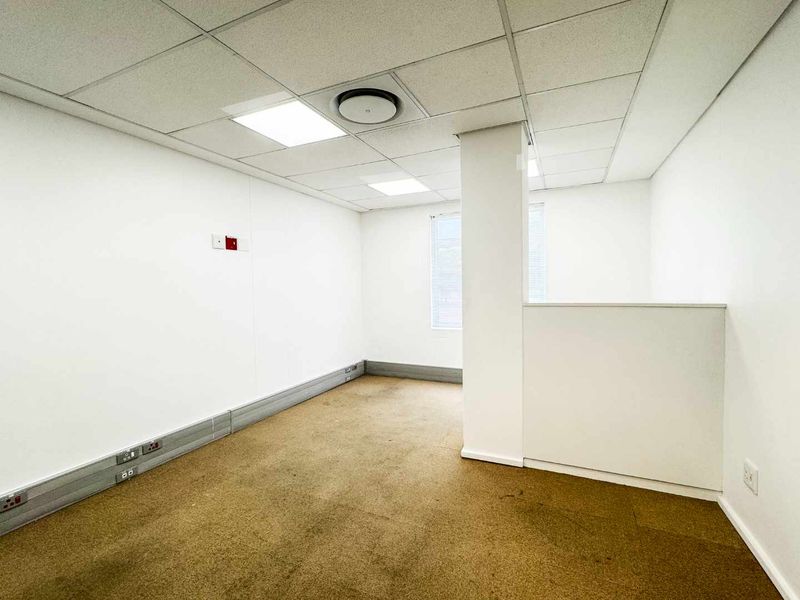 An empty, open-plan office space featuring a suspended ceiling with recessed lighting, carpeted flooring, and integrated wall-mounted electrical and data trunking.