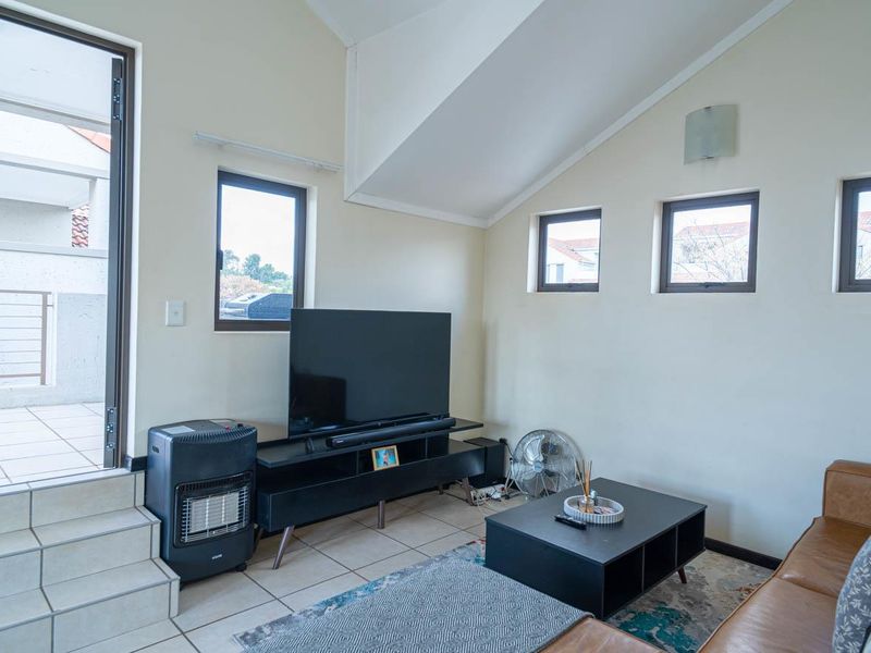 A living room featuring vaulted ceilings, tiled flooring, and direct access to an outdoor patio area through a glass door.