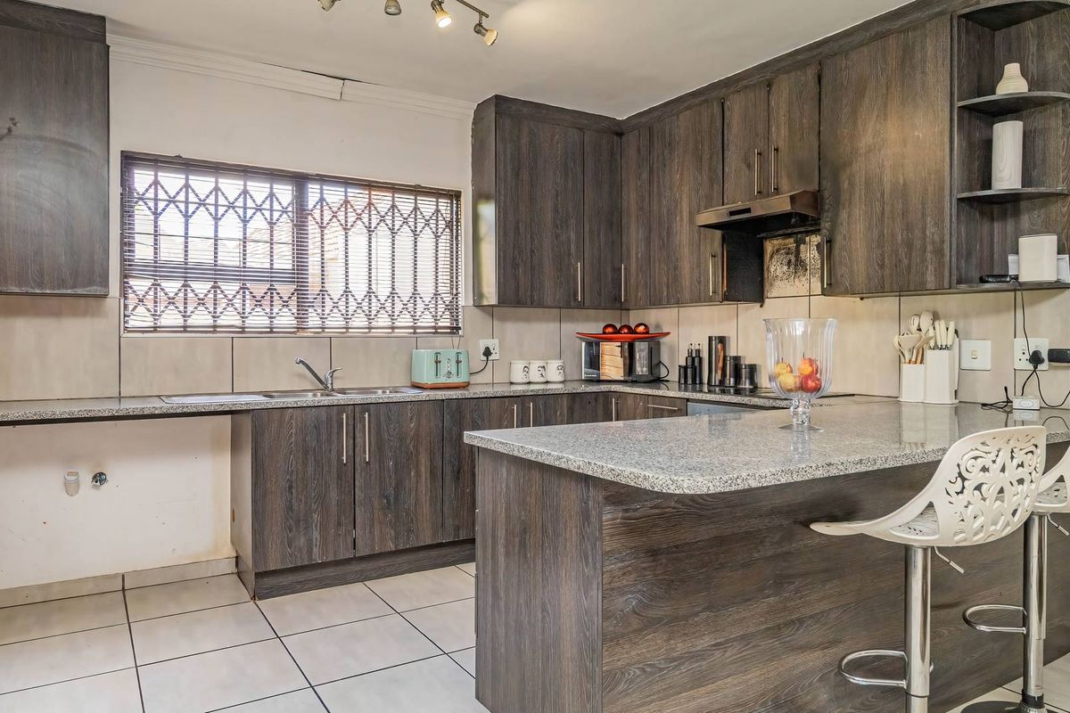 A functional kitchen featuring dark wood-look cabinetry, granite countertops, a breakfast nook, and tiled flooring, with a security-fitted window.