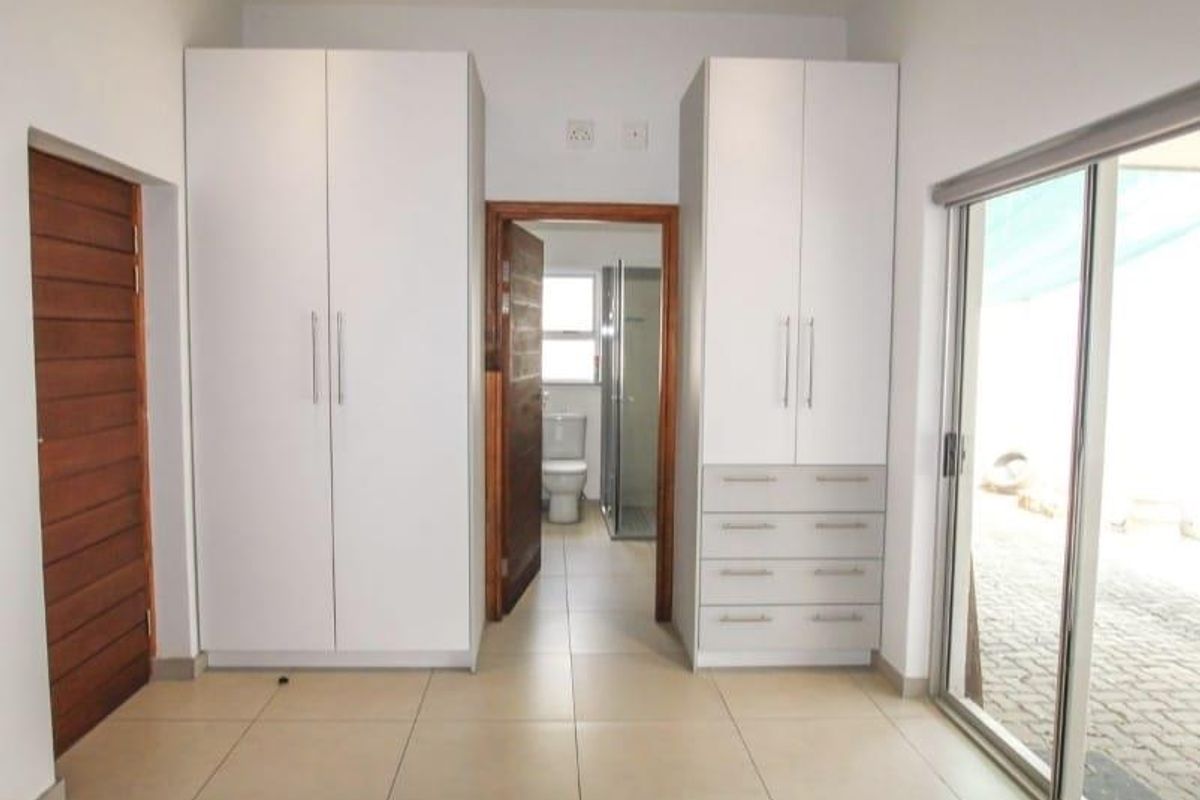 A bright bedroom featuring built-in cupboards, tiled flooring, and direct access to an en-suite bathroom with a shower.