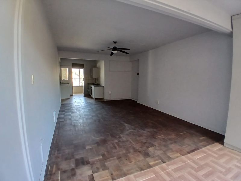 An open-plan living and kitchen area featuring parquet flooring, a ceiling fan, and a functional kitchen space with built-in cabinetry.