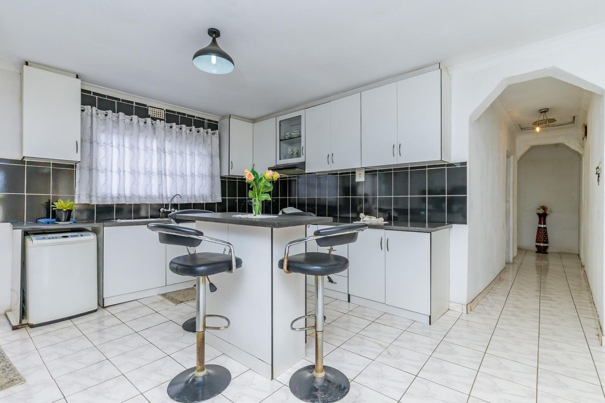 A functional kitchen featuring white built-in cabinetry, a central island, black tiled backsplash, and ceramic floor tiles.